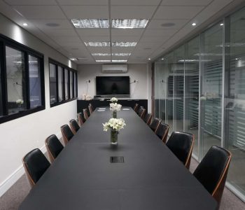Sala de reunião Herus Hiru na sede Fismatek, com mesa para 16 pessoas e estrutura de vidro.
