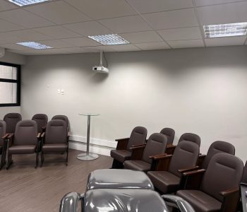 Sala Francisco, auditório de treinamentos da Fismatek com poltronas reclináveis, projetor e maca de equipamento em primeiro plano