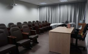 Vista lateral da Sala Francisco com fileiras de poltronas para treinamento e maca de equipamento ao fundo